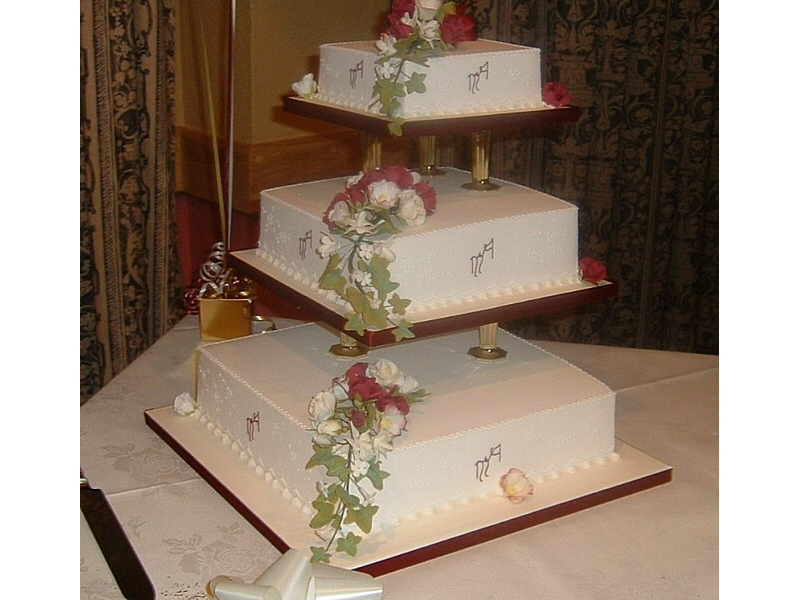 Annette - 3 tier off-set square cream royal iced, pillared wedding with trailing ivy, roses and monograms of the bride and groom from Bolton